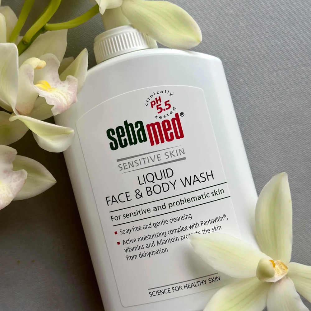 Sebamed liquid face and body wash bottle with white flowers on a gray background