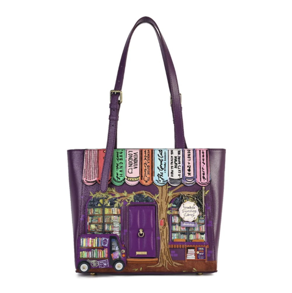 A purple faux-leather tote bag featuring a whimsical library storefront illustration on the front, complete with book spines, a tree trunk, shelves, and a purple door, shown against a plain white background.