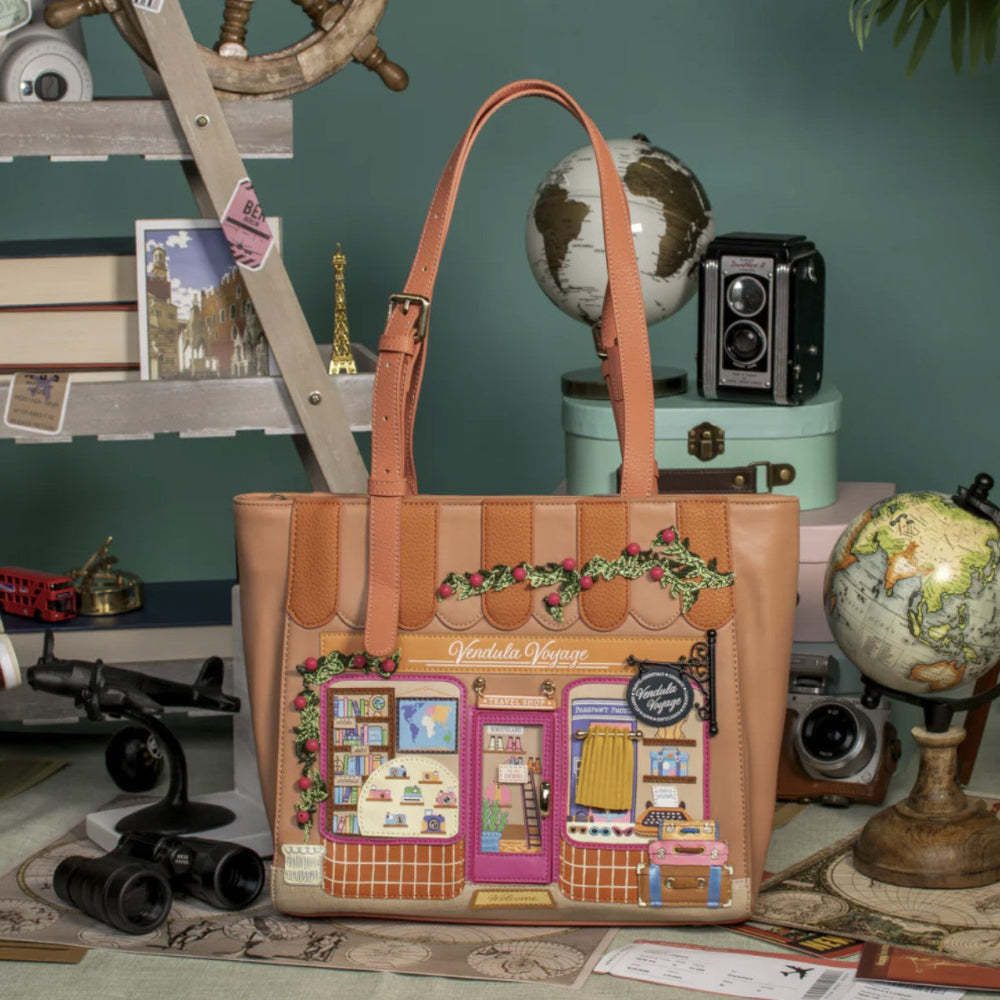 Tan tote bag with decorative design of a store front on a desk with globes and books.