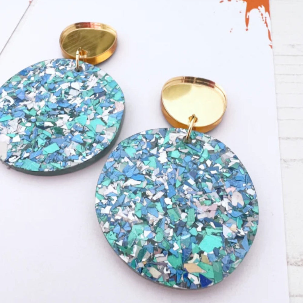 Pair of round earrings with blue and gold accents on a colorful background