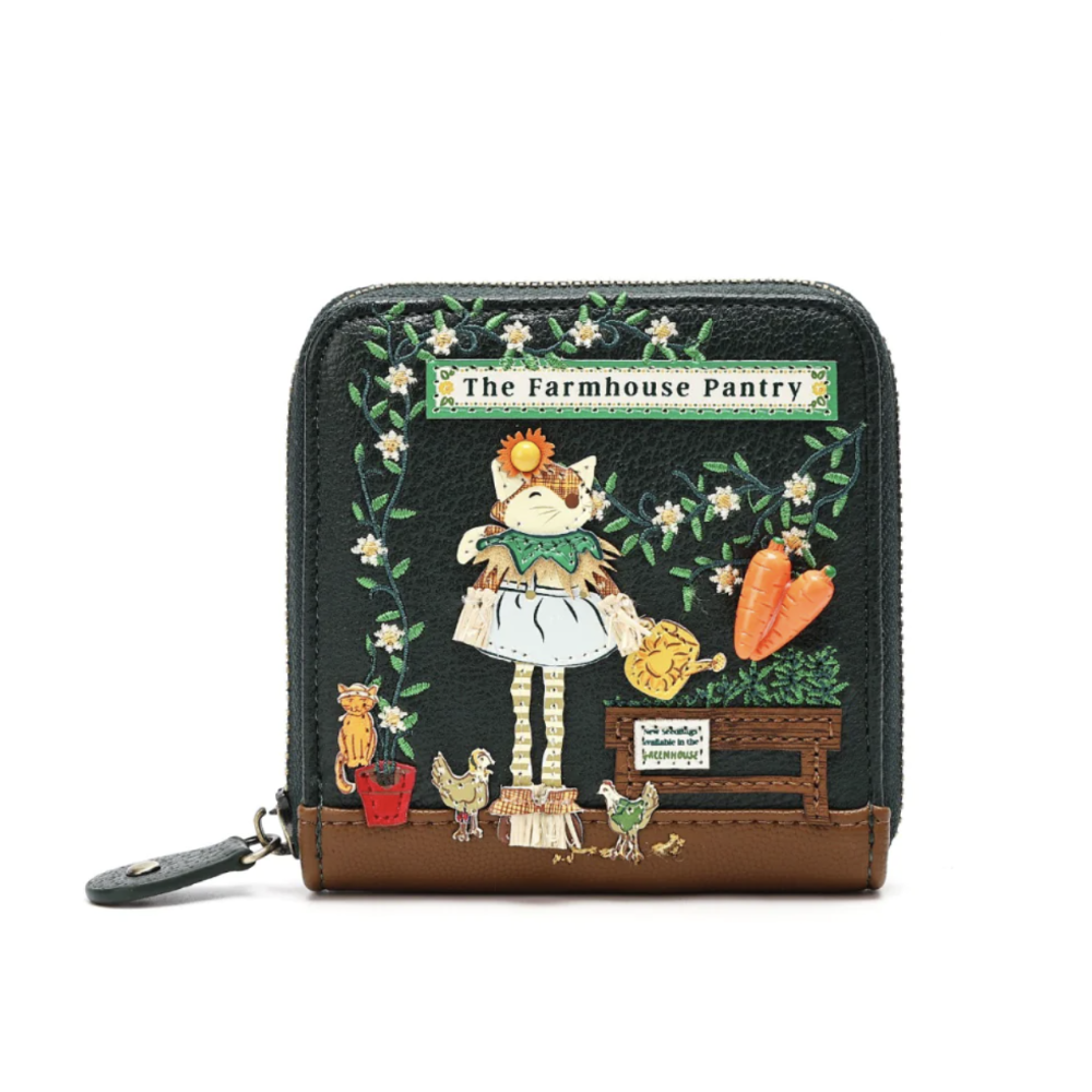 A small zip-around wallet with a dark green textured faux-leather body and a brown leather base. The front features a whimsical embroidered-style illustration of a girl in a white dress among flowers, carrots, and farm animals, with a sign reading 'The Farmhouse Pantry.