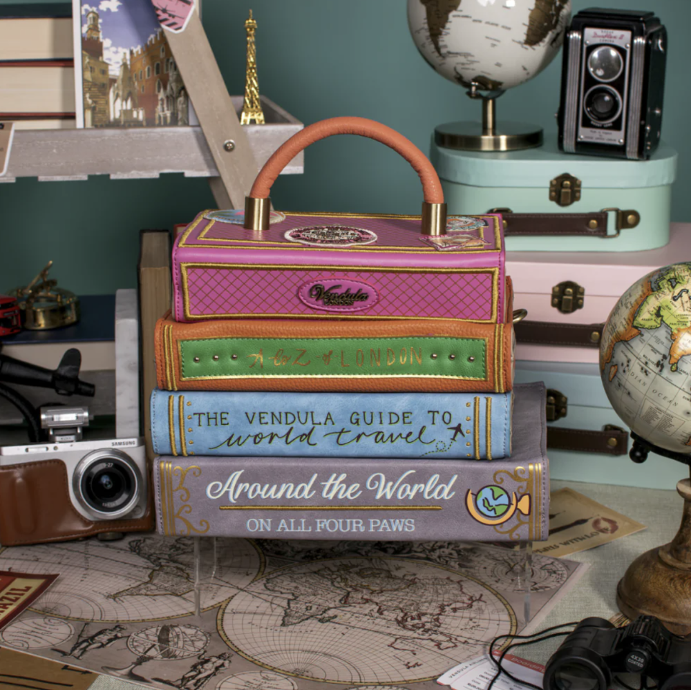 Stack of books with a decorative box on top, surrounded by travel-themed items.