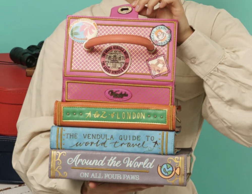 Person holding a decorative book set bag with travel-themed design against a teal background