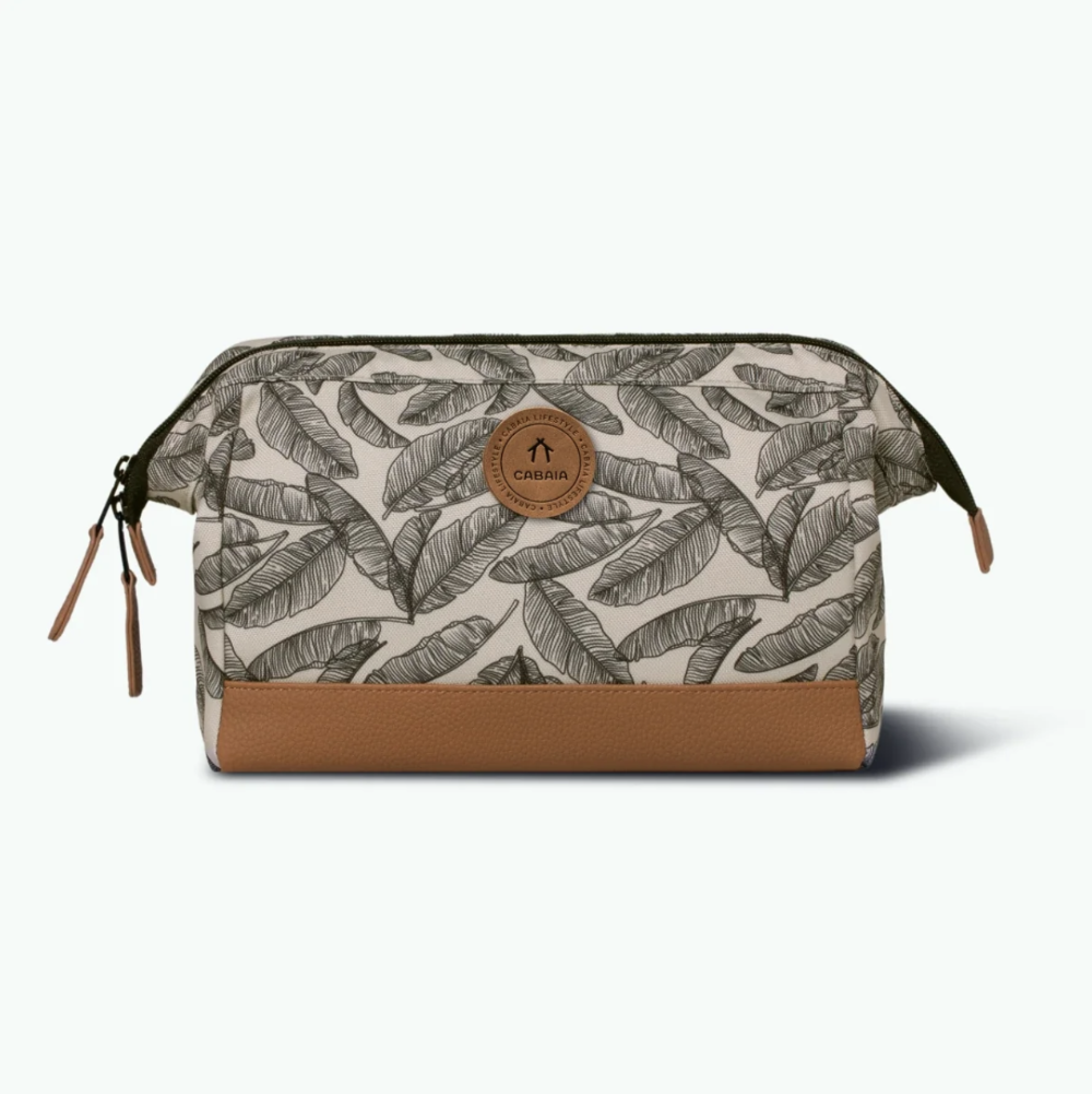 A rectangular zippered pouch with a beige and brown tropical leaf print, featuring a solid brown faux-leather bottom panel and a circular brown brand patch on the front.