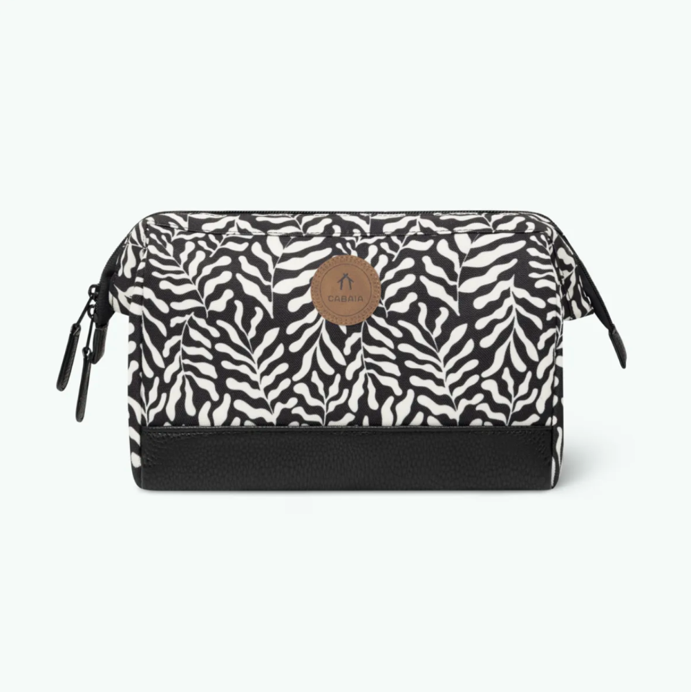 A rectangular cosmetic pouch with a black and white print pattern, a solid black base, and a circular brown leather logo patch on the front. The pouch is shown against a plain white background.