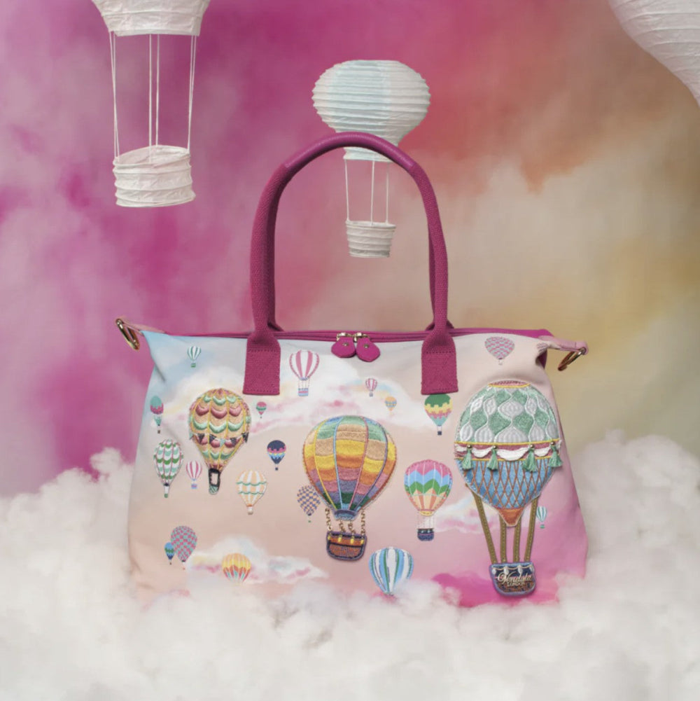 Handbag with hot air balloon design on a fluffy white surface with a pink and purple gradient background.