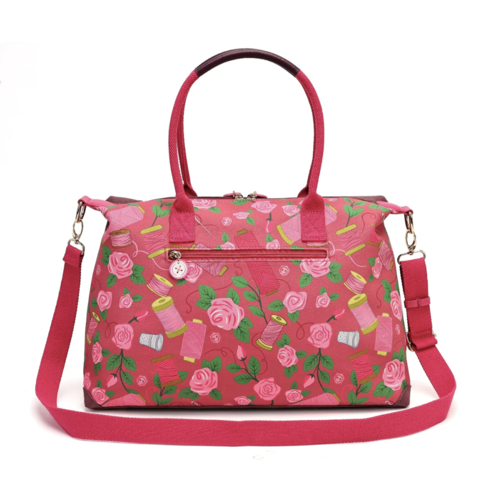 A pink handbag with a floral and sewing thread spool pattern, featuring two top handles, a front zippered pocket with a decorative charm, and an adjustable shoulder strap, shown on a plain white background.