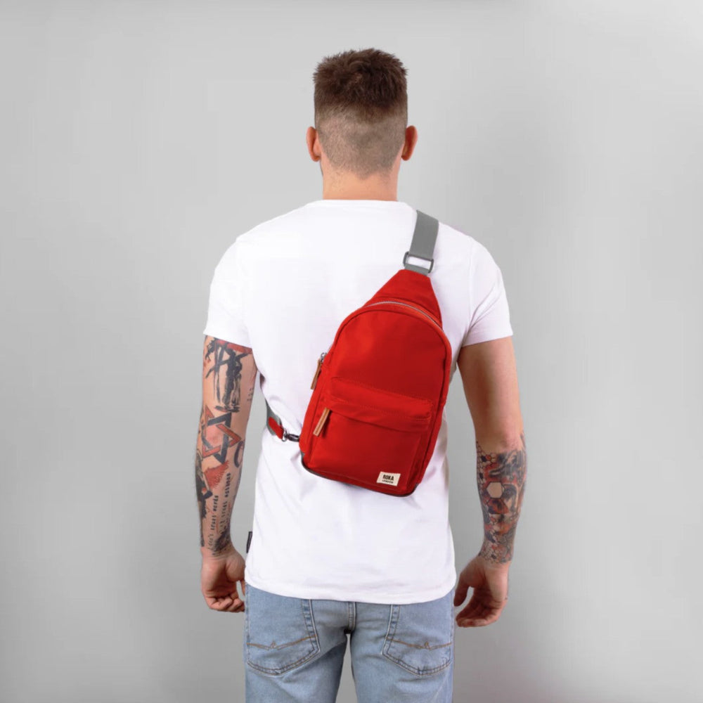 Person wearing a red sling bag on a gray background