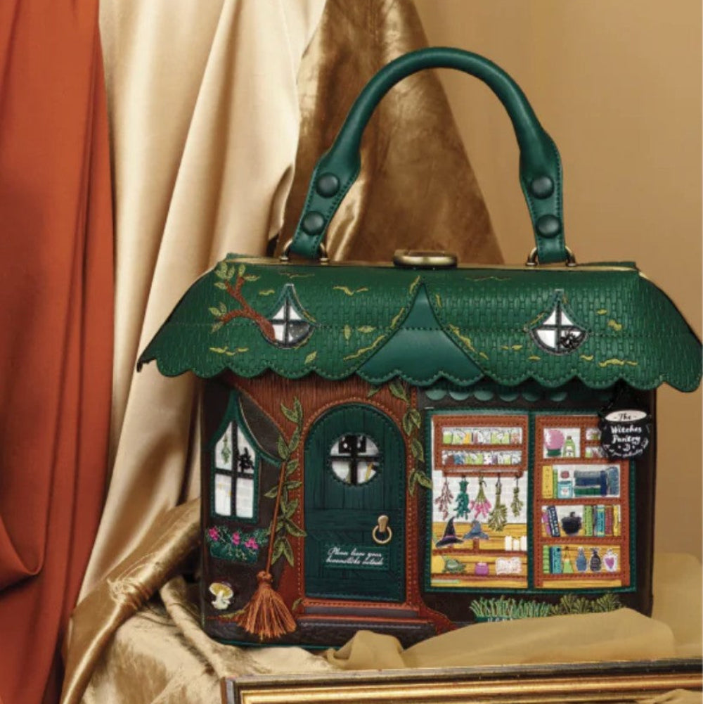 Handbag designed like a miniature house with a green roof and detailed facade on a gold fabric background.