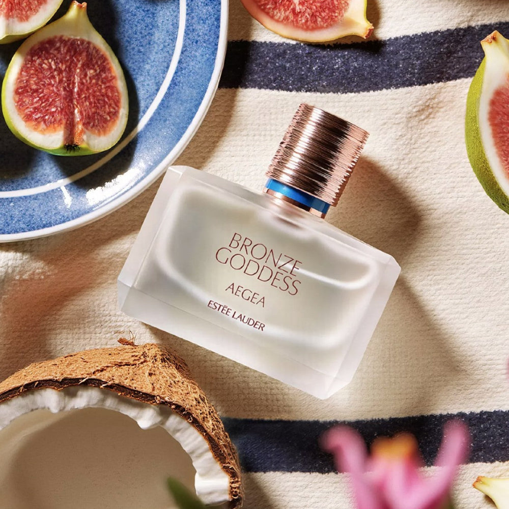 Estee Lauder Bronze Goddess Aegea Eau De Parfum with coconut & figs displayed with it on beach towel