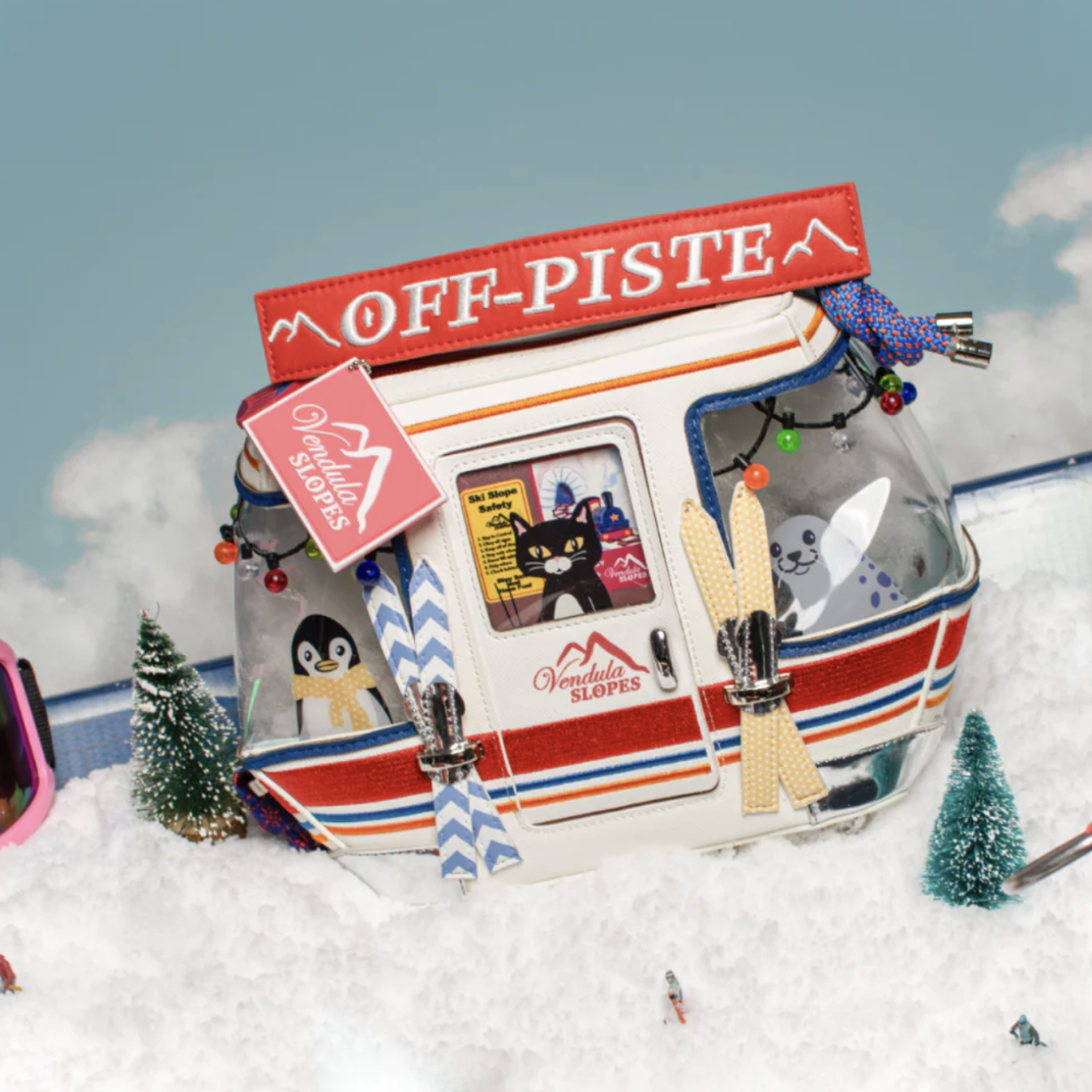 A novelty clear plastic bag shaped like a snow gondola, labeled 'OFF-PISTE' and 'Vendula Slopes,' decorated with penguin and cat stickers, set in a snowy miniature scene.