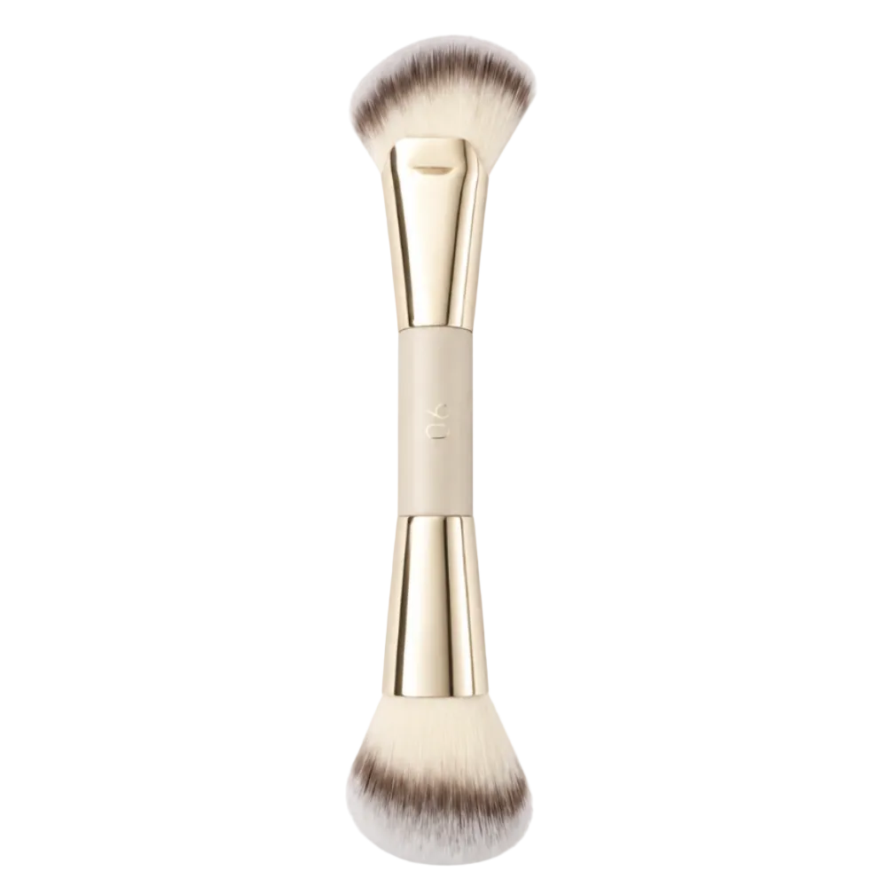 A dual-ended makeup brush with soft cream and brown bristles, a beige handle, and shiny gold metal ferrules, shown vertically on a plain white background.