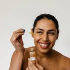 Woman applying a dropper of skincare product to her face with a white background