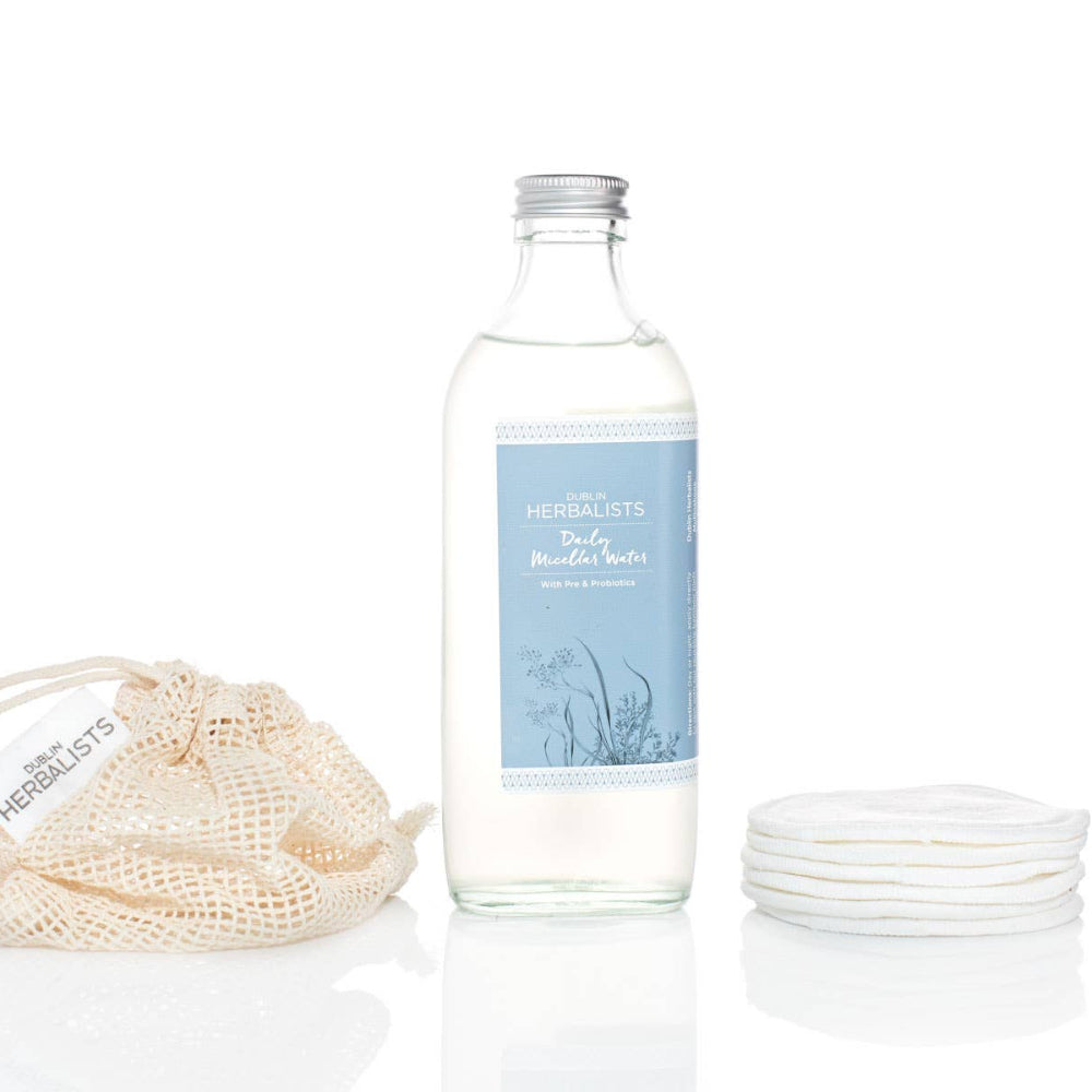 Clear glass bottle with a blue label, beige drawstring bag, and small white bowls on a white background
