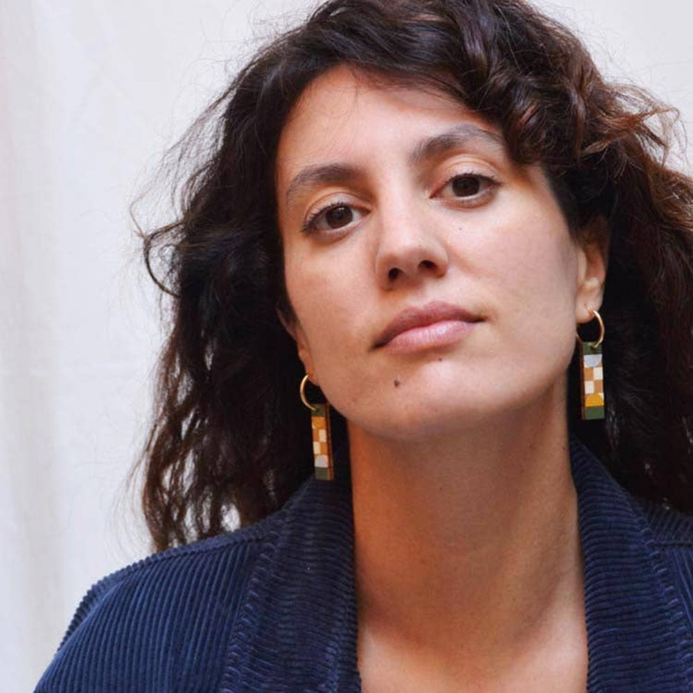 Woman wearing a navy blue jacket with hoop earrings against a neutral background