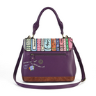 A purple leather handbag with a colorful book spine pattern across the top flap, a brown suede-like base, and a purple shoulder strap, shown on a white background.