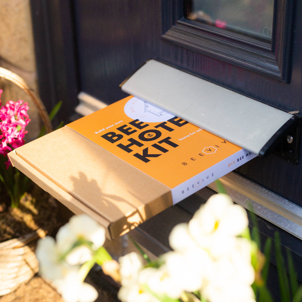 Bee Hot Kit package attached to a door with flowers in the foreground