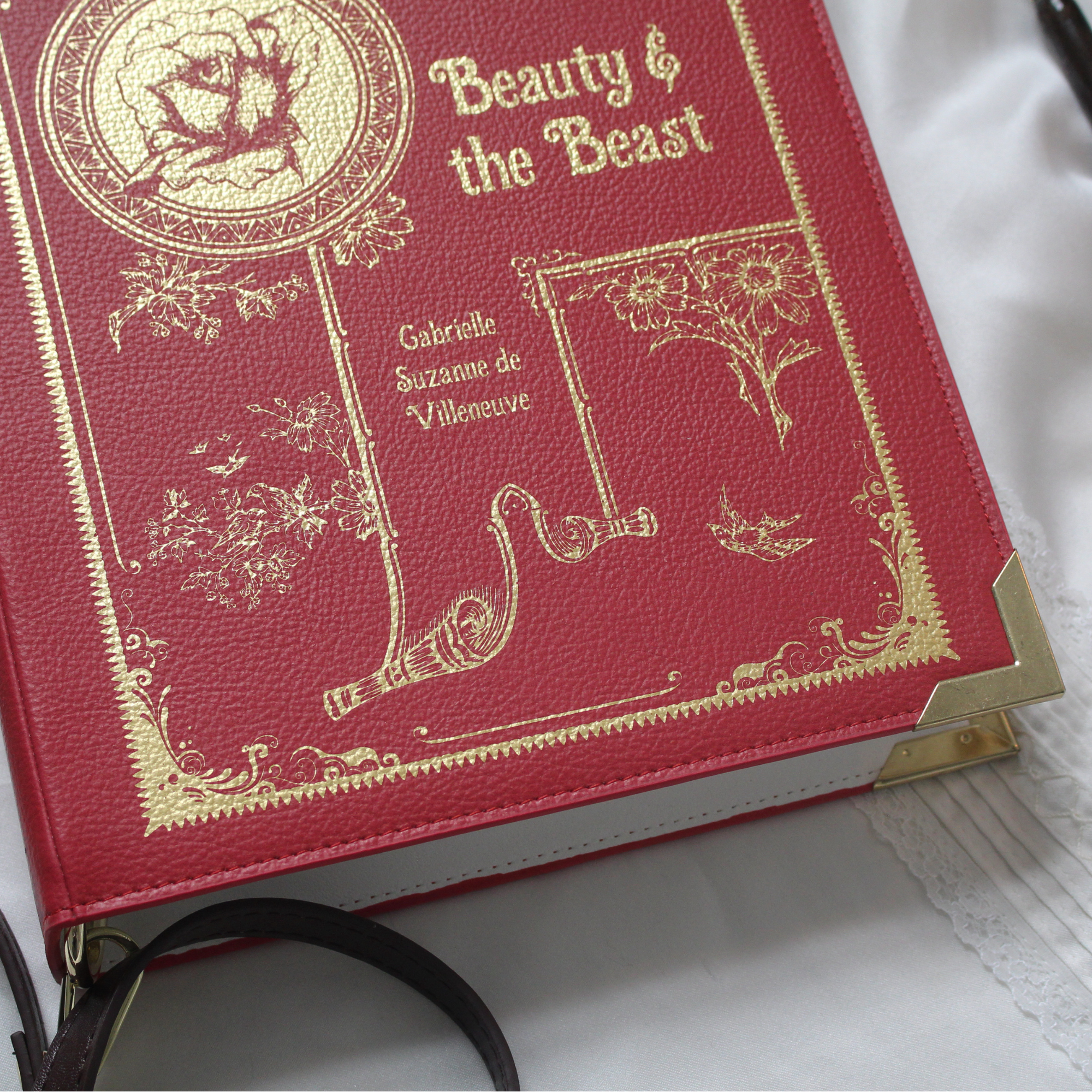 A red faux-leather crossbody bag designed to look like a vintage 'Beauty & the Beast' book, shown on a white background.