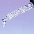 Glass dropper with clear liquid against a light purple background