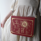 A red faux-leather crossbody bag designed to look like a vintage 'Beauty & the Beast' book