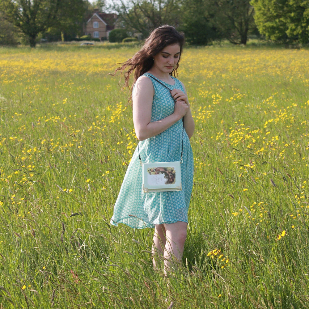Woman in a green dress standing in a field of yellow flowers, holding a handbag.