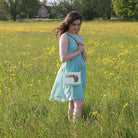 Woman in a green dress standing in a field of yellow flowers, holding a handbag.