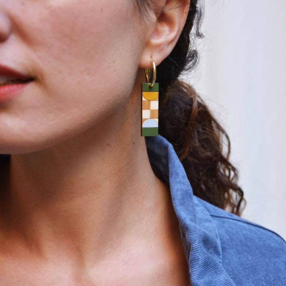 Close-up of a person wearing colorful geometric earrings with a blurred background