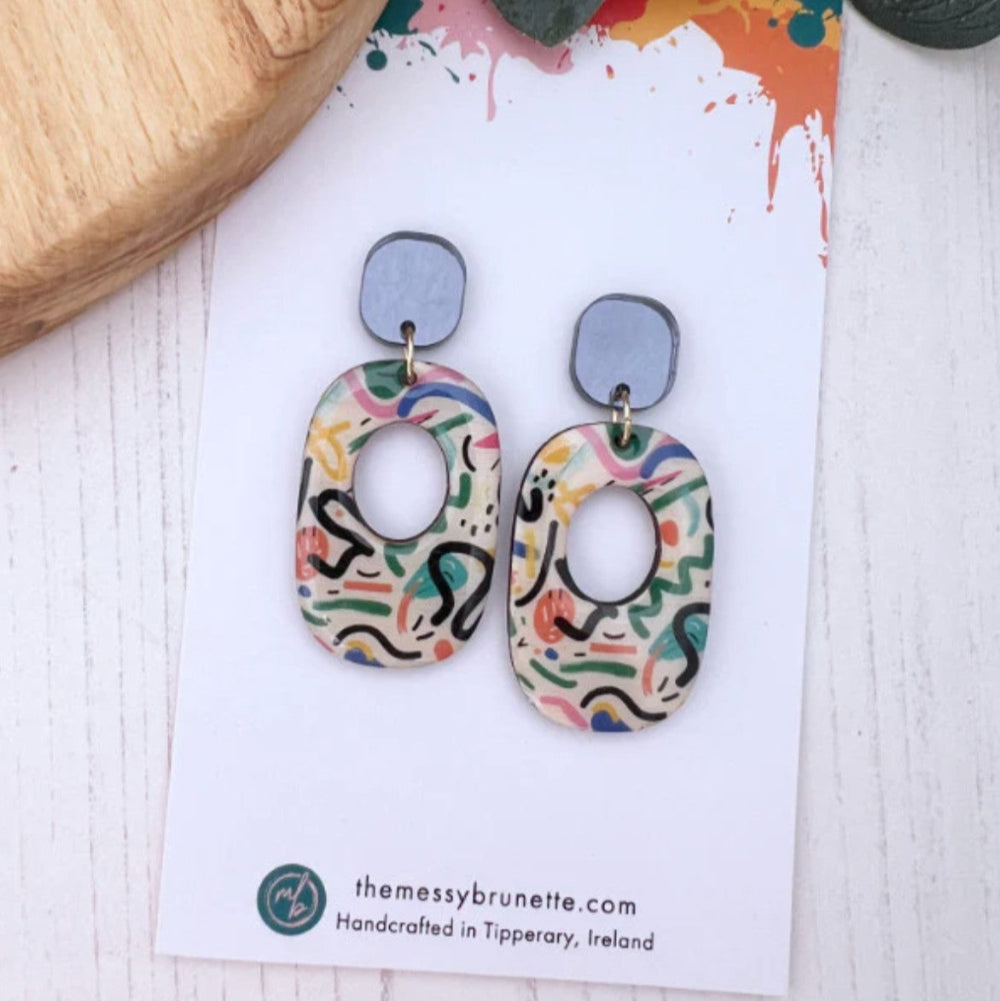 Colorful abstract patterned earrings on a branded card with 'the messy brunette' branding.