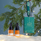 Two skincare bottles and a box labeled 'Winter Glow Duo' hanging from a tree branch with snow and lights in the background.