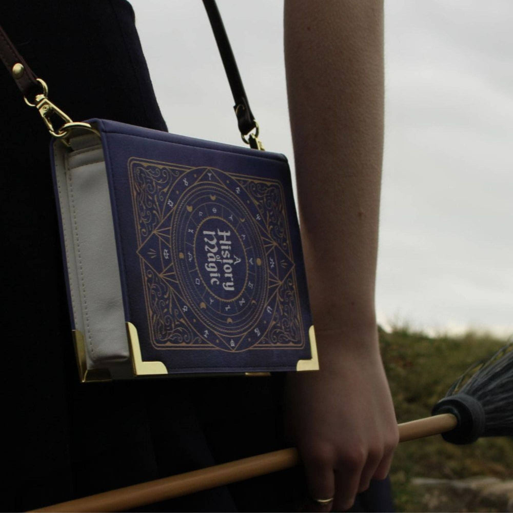 Book-shaped handbag with 'History of Magic' design held by a person outdoors.