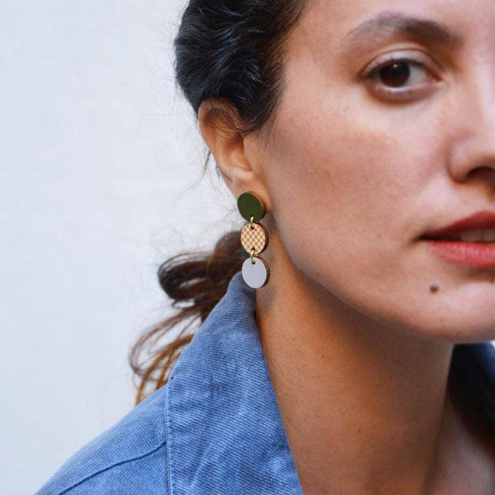 Close-up of a person wearing green earrings with a plain background