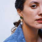 Close-up of a person wearing green earrings with a plain background