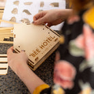 Person assembling a wooden bee hotel with a floral-patterned sleeve in the foreground.