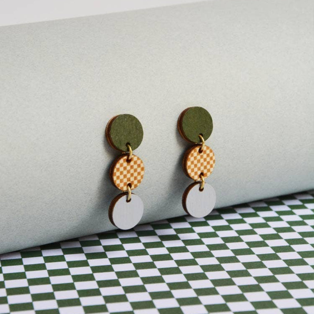 Pair of earrings with green, gold, and white circular components on a checkered surface.