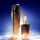 Two Estée Lauder Advanced Night Repair skincare bottles on a reflective surface against a blue gradient background with light effects. The larger bottle on the left is a tall recovery treatment essence bottle, and the smaller dropper bottle on the right is the advanced night repair serum.
