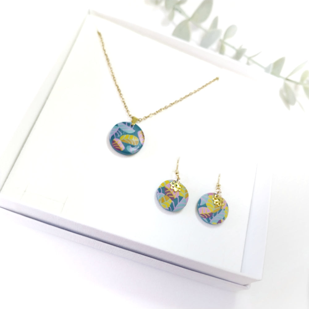 Colorful floral earrings and necklace on a white surface with green leaves in the background