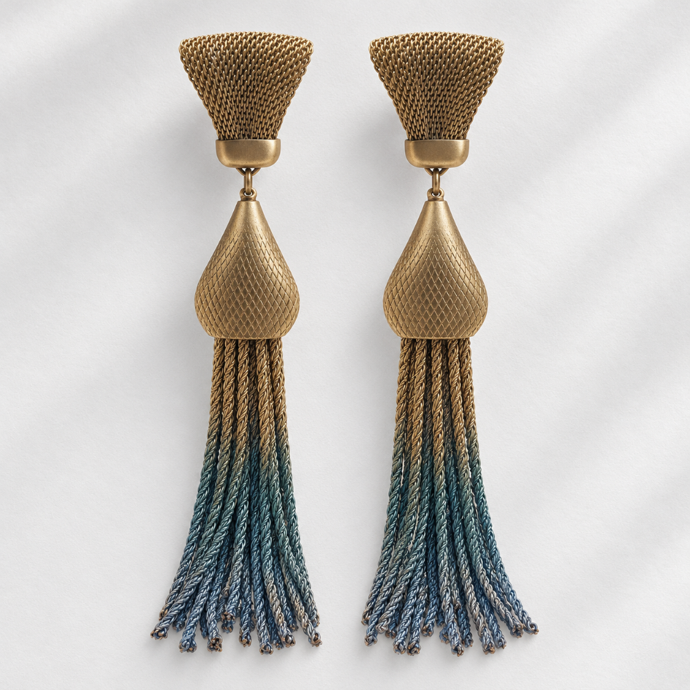A pair of statement dangle earrings with textured gold-tone metal tops and teardrop-shaped links, featuring braided tassels that transition from gold at the top to blue at the bottom, set against a light gray background with soft shadows.