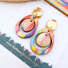 Colorful earrings on a white surface with a branded card underneath