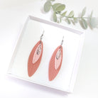 Pink feather-shaped earrings on a white card with a green leafy branch in the background