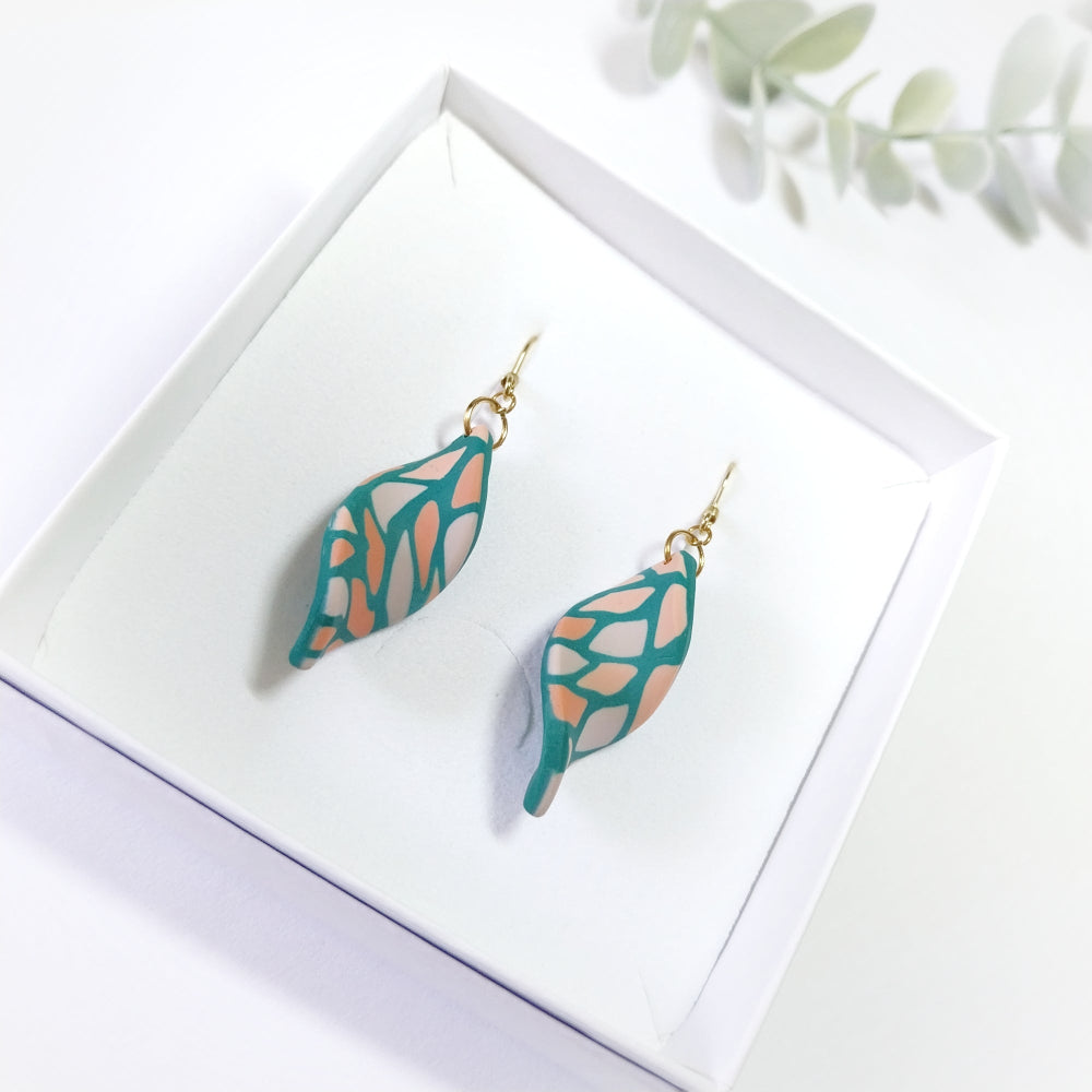 Teal and pink leaf-shaped earrings on a white box with a light background
