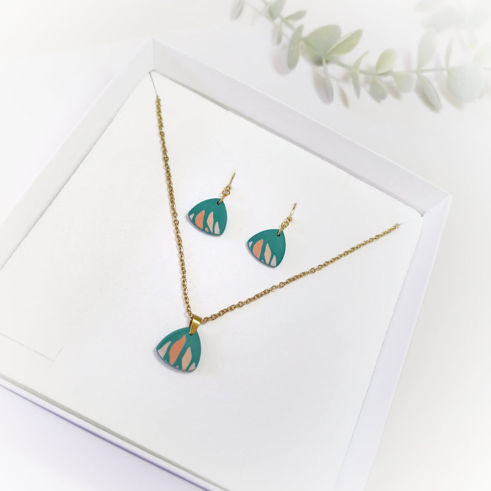 Jewelry set with necklace and earrings on a white card with green leaves.