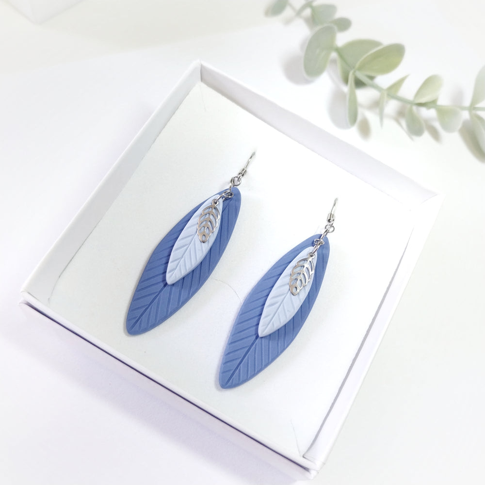 Blue feather-shaped earrings on a white box with a light background