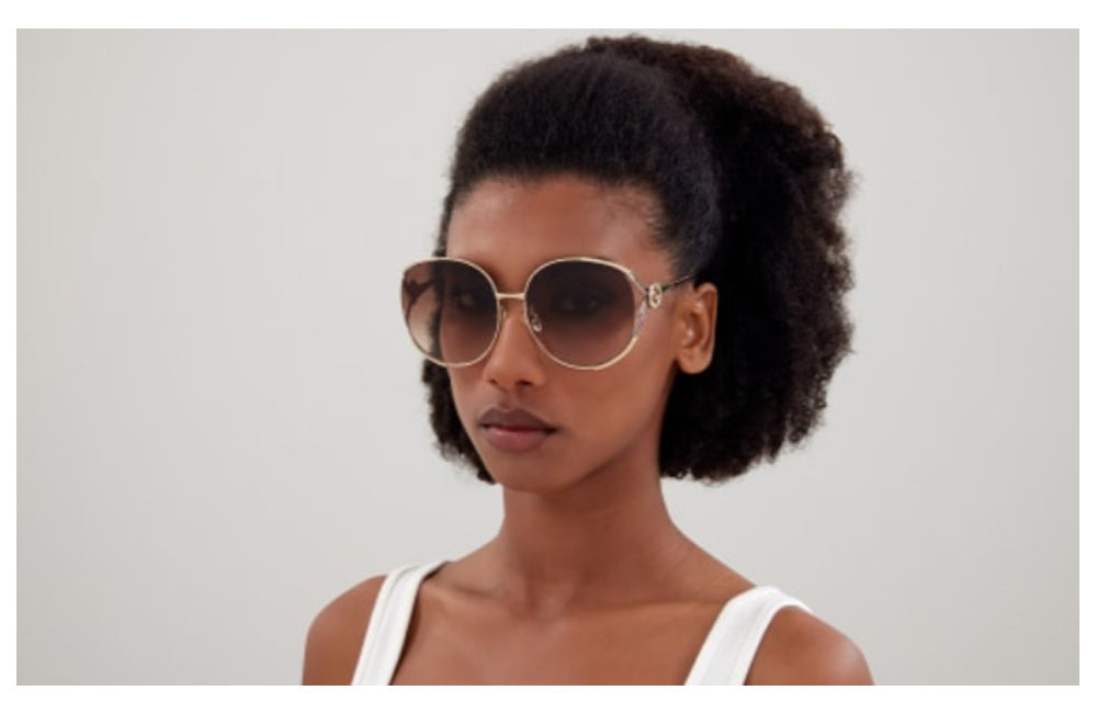 Woman wearing Gucci large gold round sunglasses