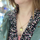 Person wearing a floral blouse with a green jacket and a gold necklace.