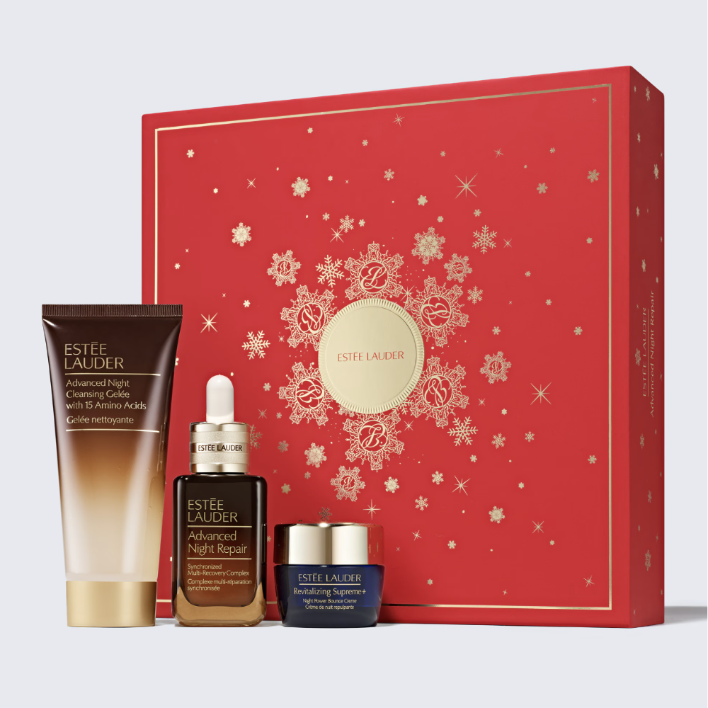 Estée Lauder holiday gift set featuring a red gift box with gold snowflake patterns and three skincare products in front: a brown and gold Advanced Cleansing Gel tube, a dark brown Advanced Night Repair Serum dropper bottle, and a dark blue Revitalizing Supreme cream jar.