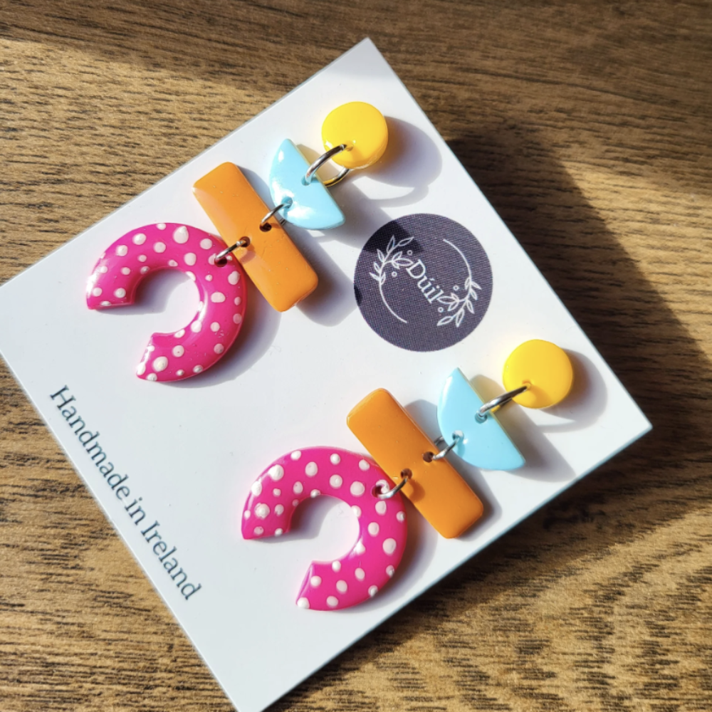 Colorful earrings on a card with 'Duil' branding on a wooden surface