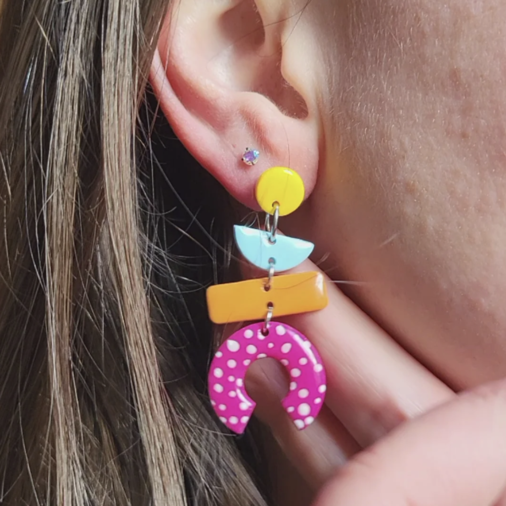 Colorful earrings being worn with a close-up of the ear and hair.