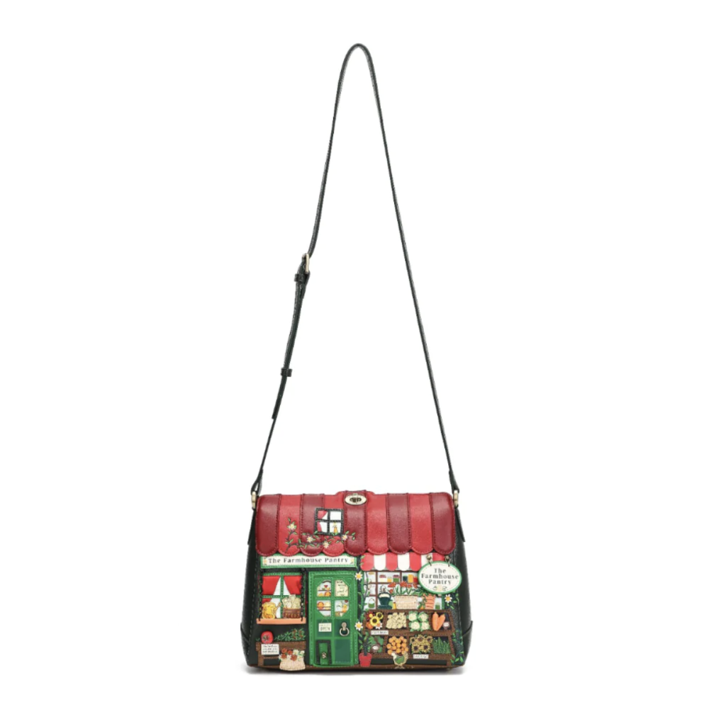 A small shoulder bag with a red quilted top and a colourful patchwork-style storefront print on the front, featuring a black shoulder strap, photographed on a plain white background.
