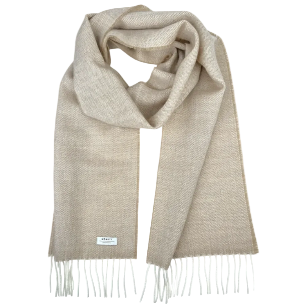 A light beige woven scarf with fringed ends, draped in a looped style on a solid white background. A small white brand label is visible near the bottom left edge.