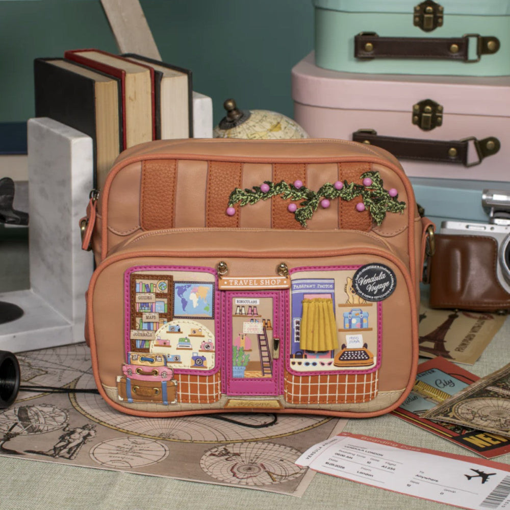 Small backpack with illustrated front panel on a surface with books and a camera in the background